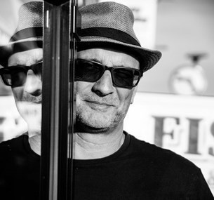 Black and white headshot of Mark Curryer with a partial reflection in a window