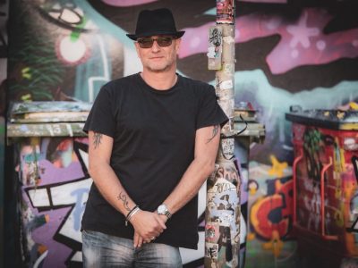 Mark Curryer in a black hat in front of a graffiti wall